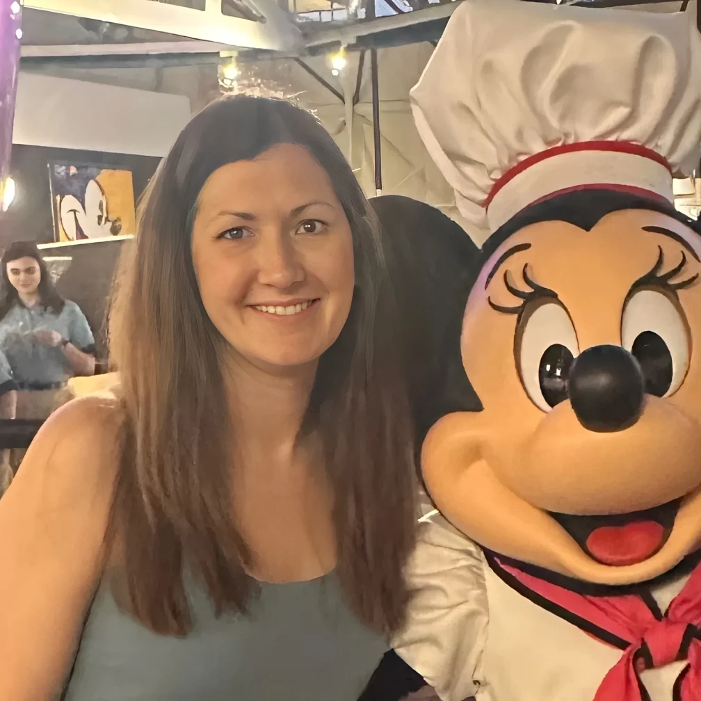 Woman smiling next to a Minnie Mouse character in a chef outfit.